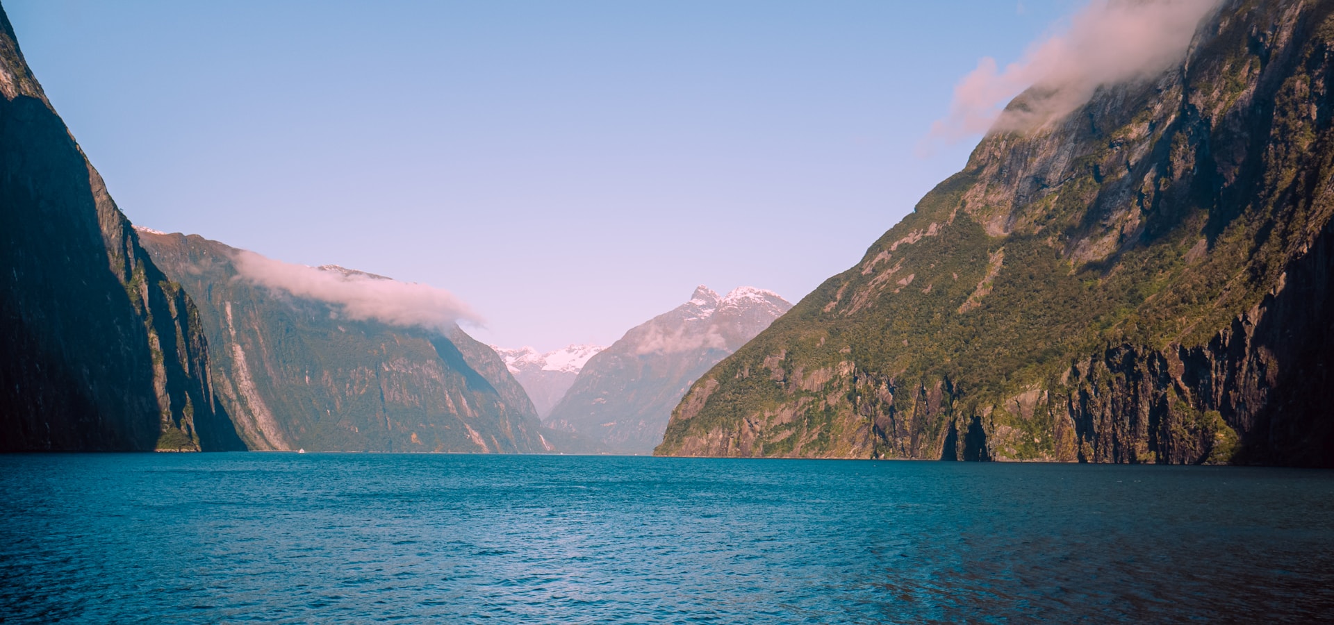 Steep green cliffs over still water in a fjord.